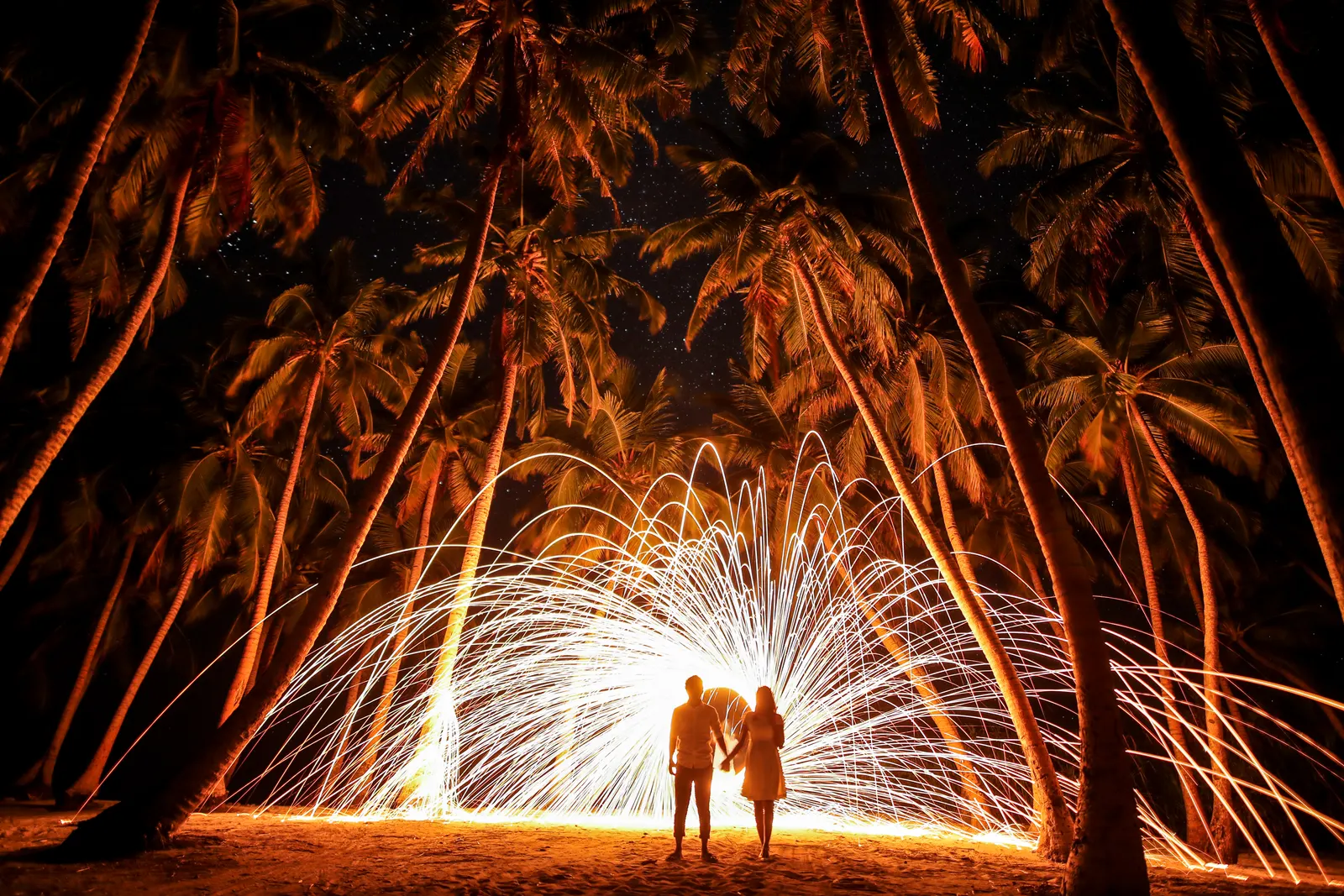 Couple under sparks on a palm beach at night