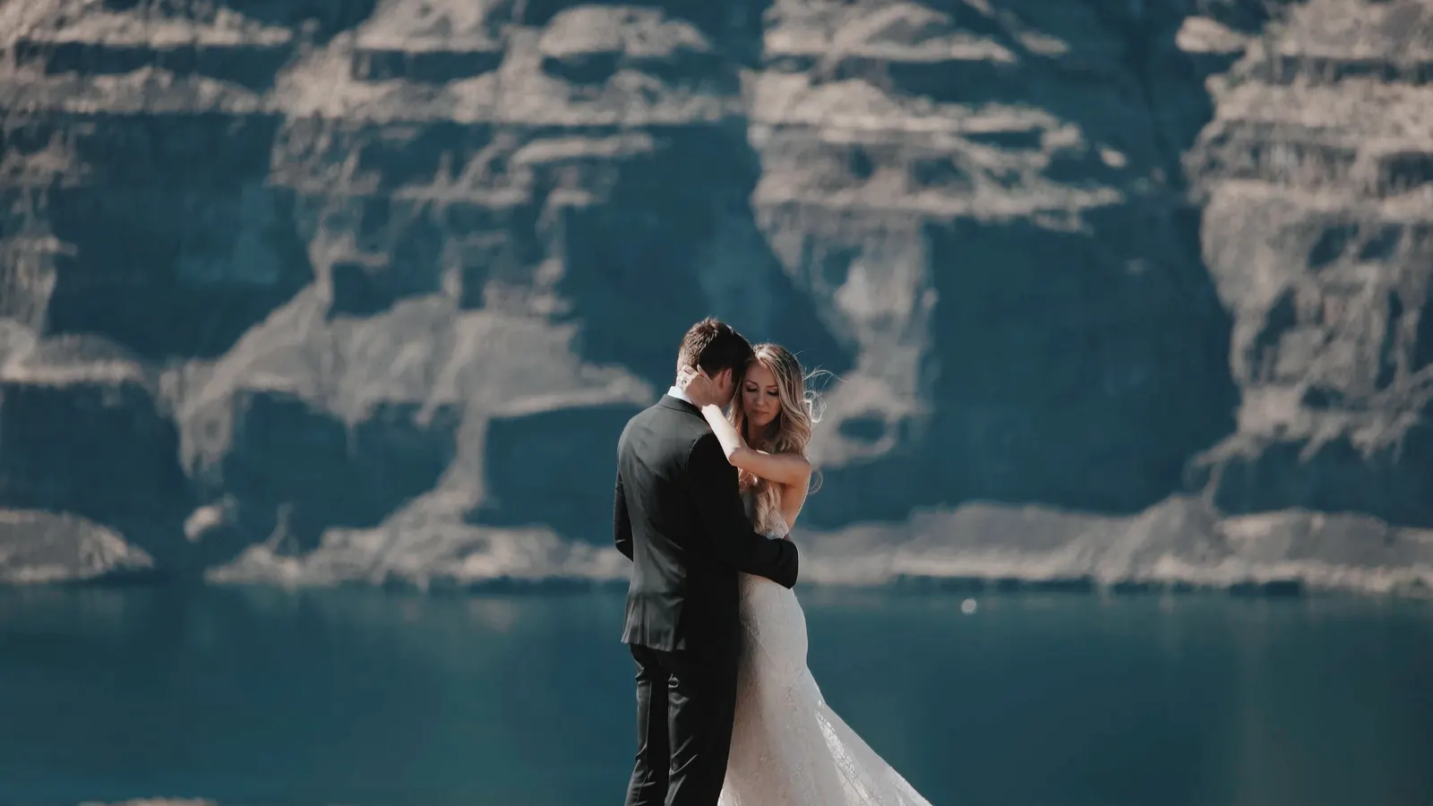 Wedding couple embracing on a cliff above a lake